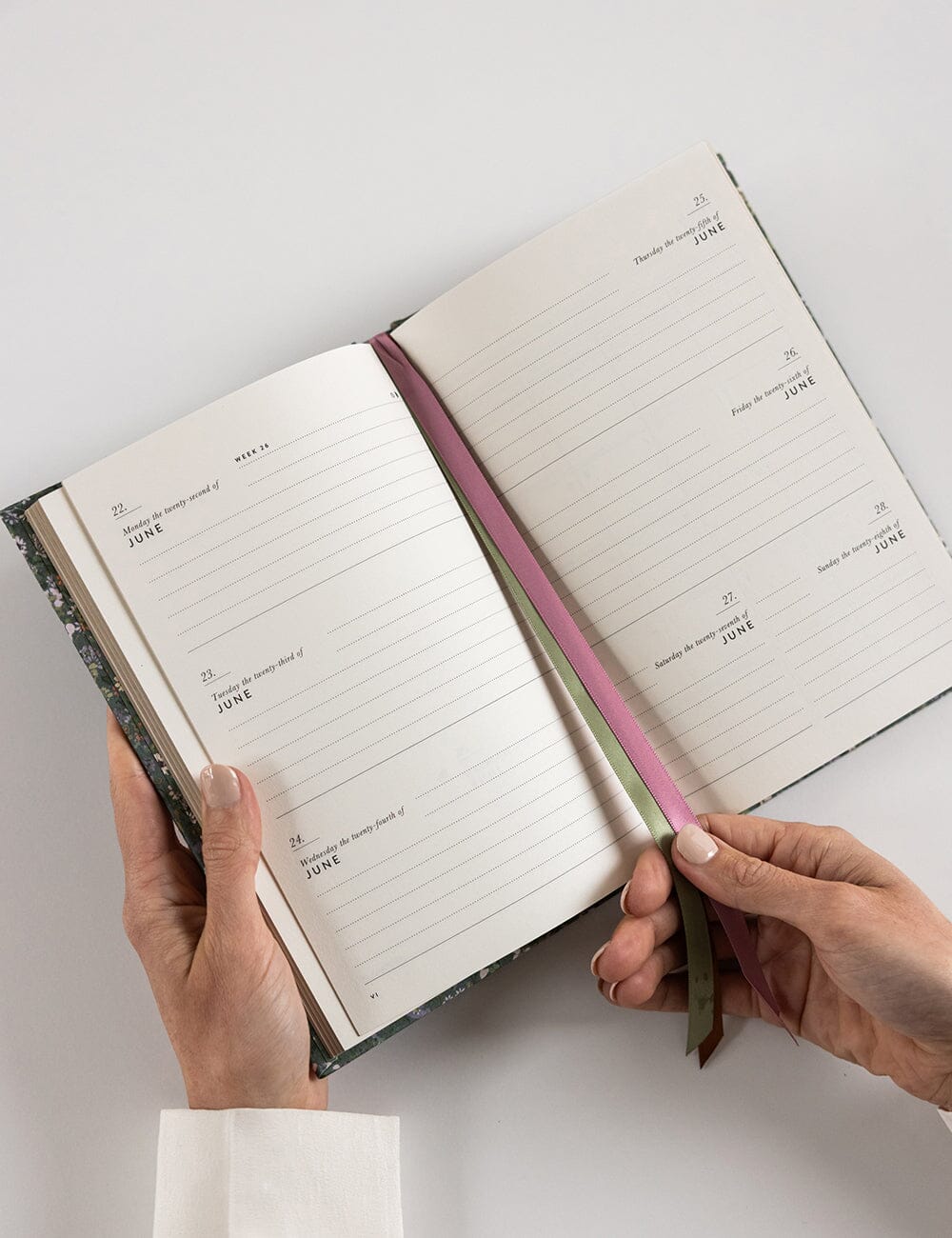 Open notebook held by hands on a light gray background