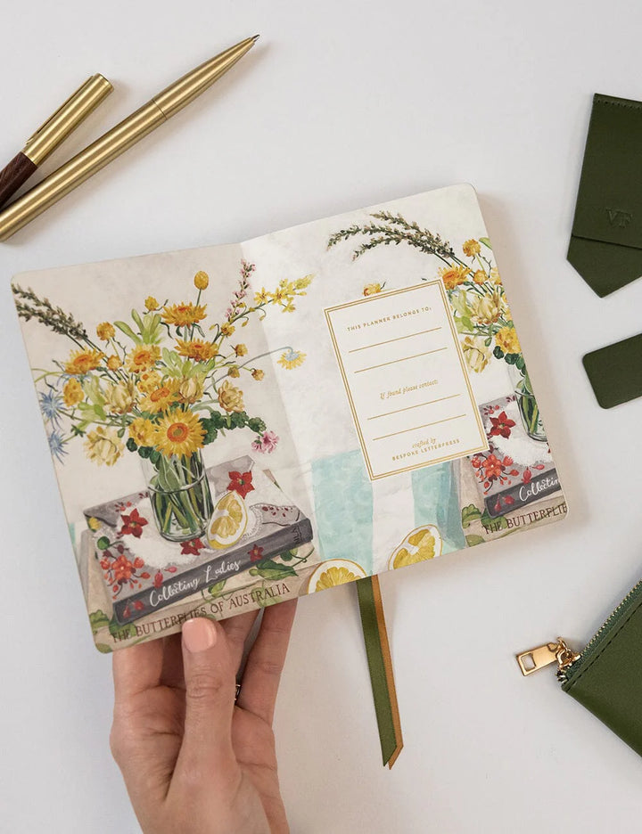 Floral notebook held by a hand with stationery items on a white background