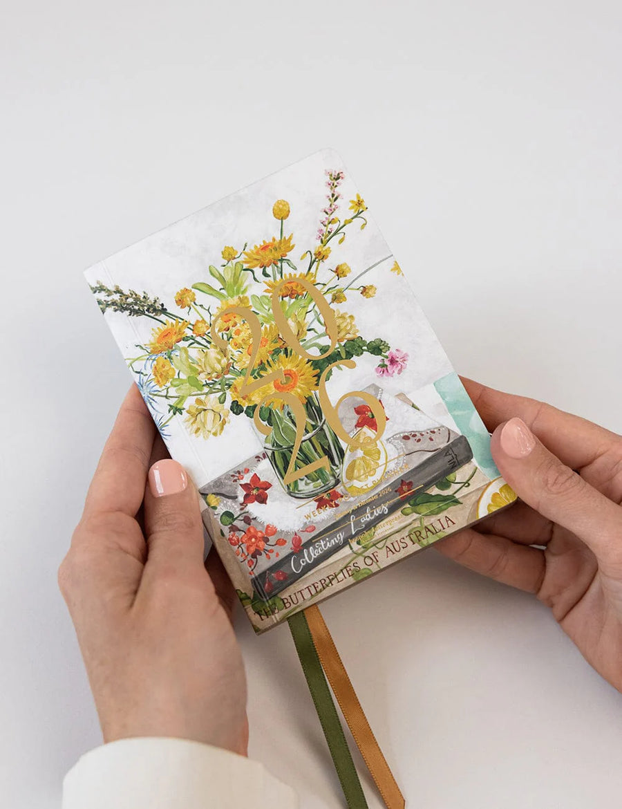 Hand holding a small notebook with floral design on a white background