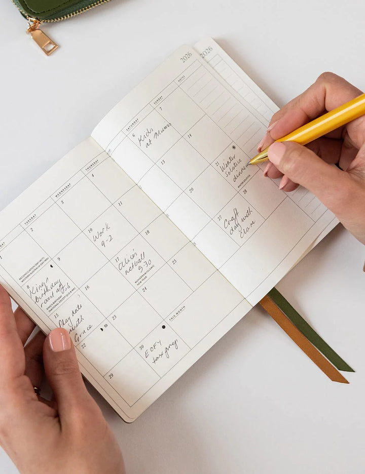 Person writing in a planner with a yellow pen on a white surface