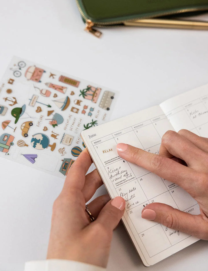 Person holding a planner with stickers on a white surface