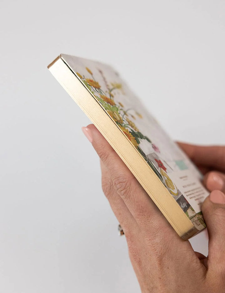 Hand holding a small rectangular object with a gold border and colorful design on a white background
