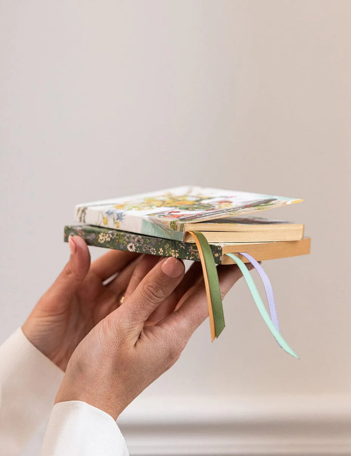 Hand holding a stack of books with a ribbon marker against a plain background