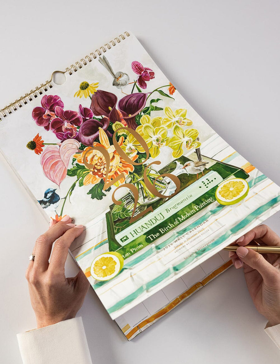 Person holding a spiral-bound planner with floral and cocktail design on a white background