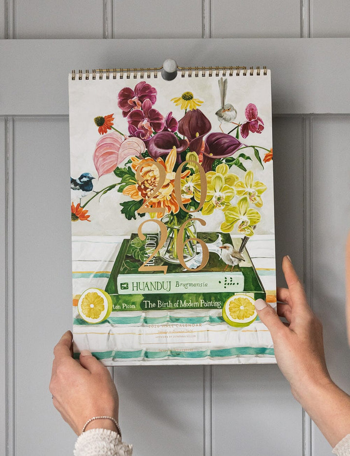 Person holding a floral-themed calendar against a gray wall