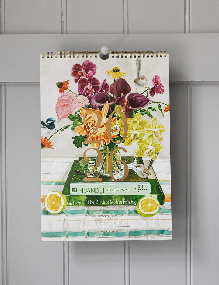 Wall calendar with floral design and brand name on a gray wall
