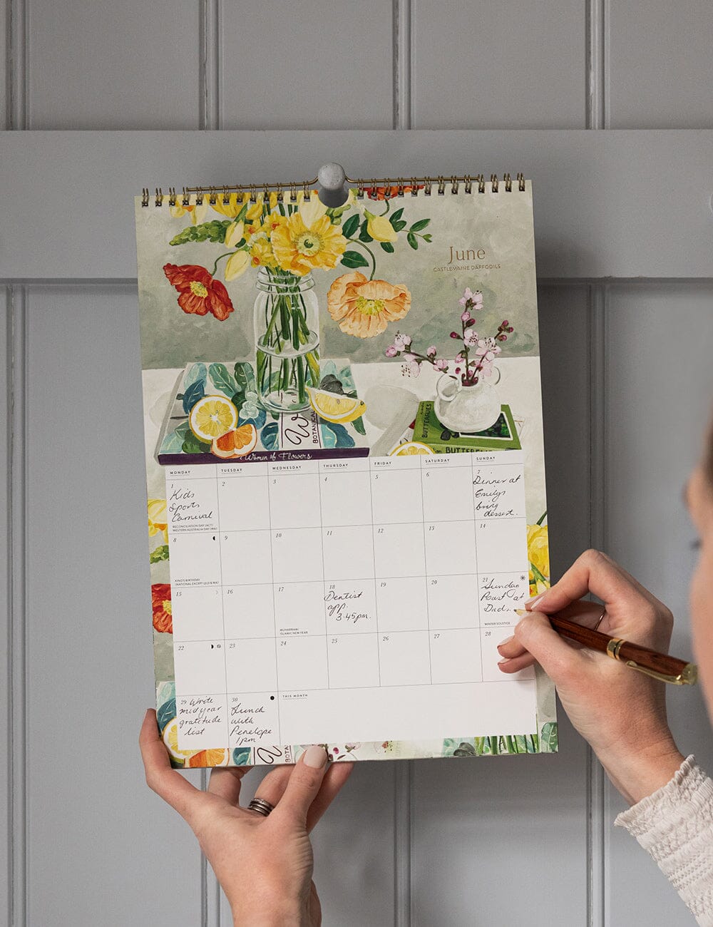 Person holding a floral-themed calendar against a gray wall.