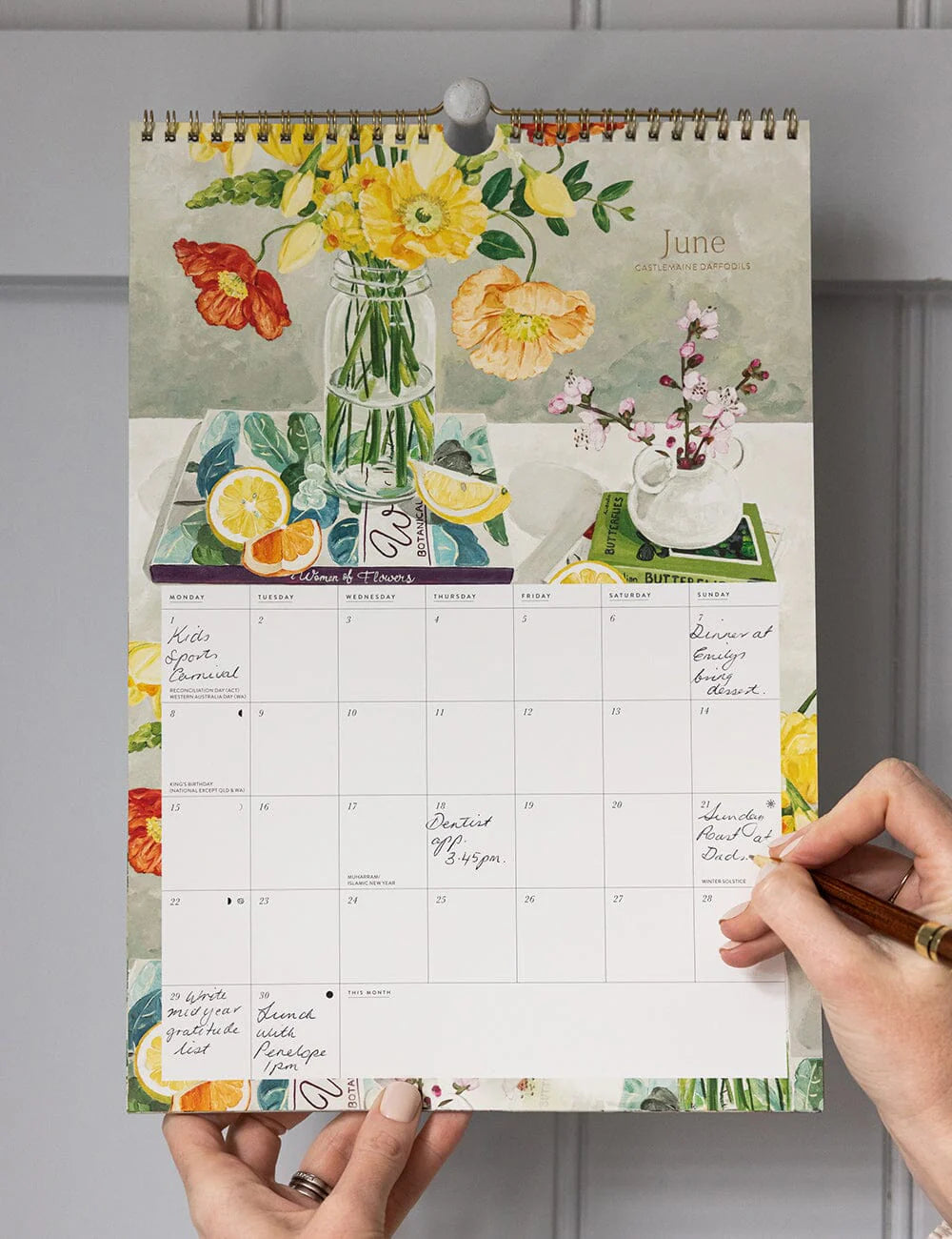Calendar with floral design held by a hand against a gray wall.