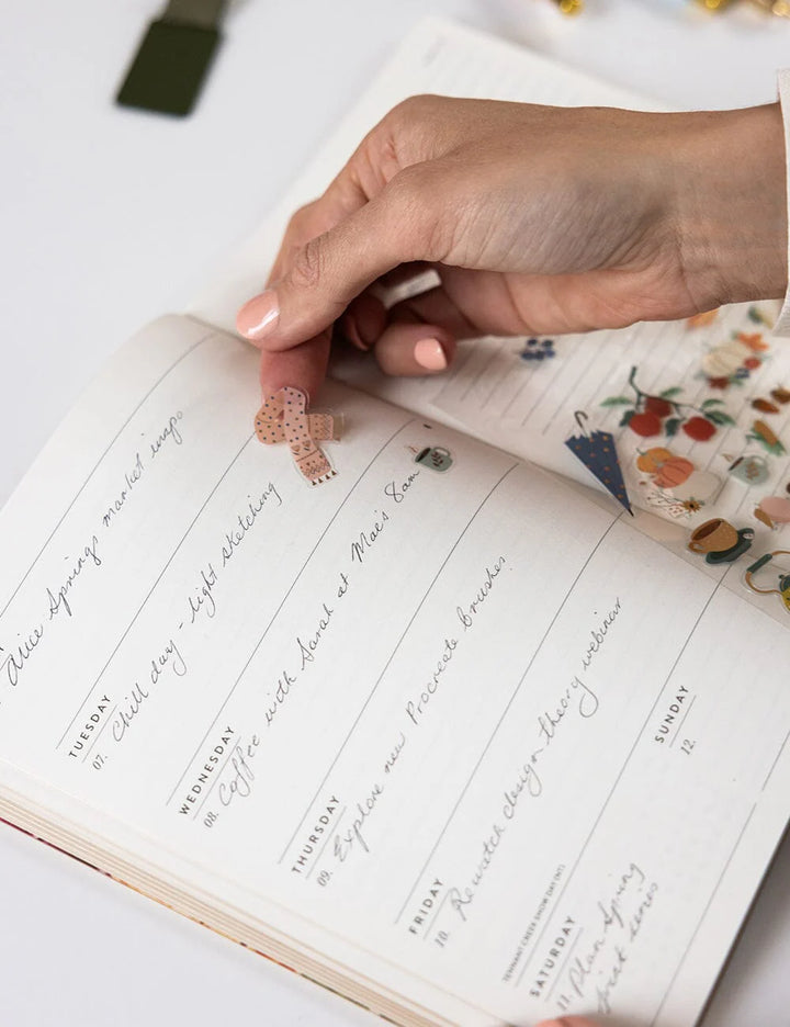 Hand holding a small decorative item over a planner with handwritten notes.