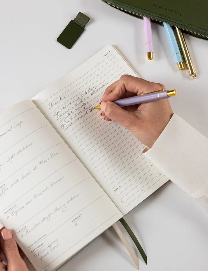 Hand writing in a notebook with colorful pens on a white surface