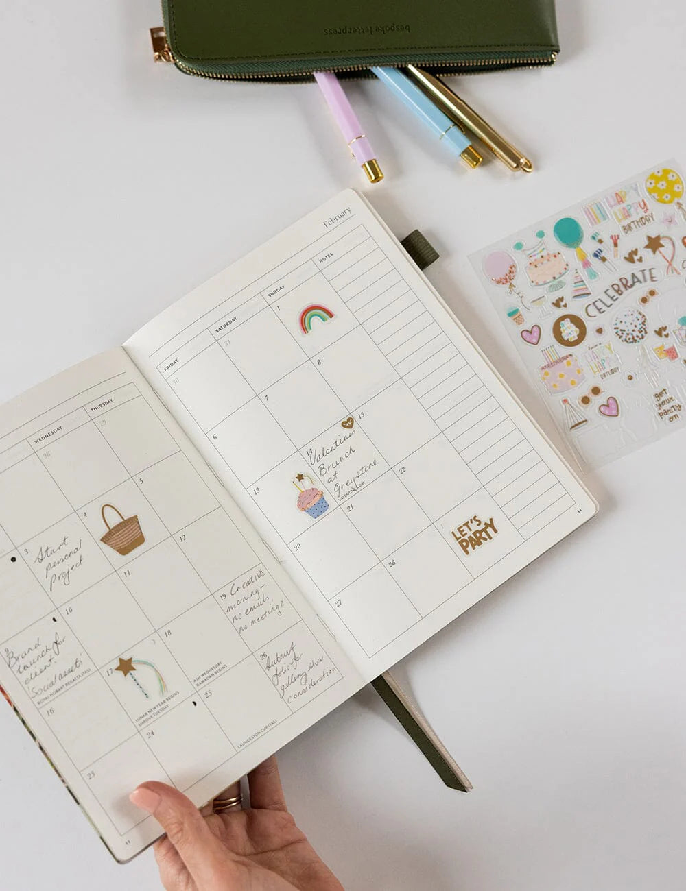 Open planner with stickers and pens on a white surface