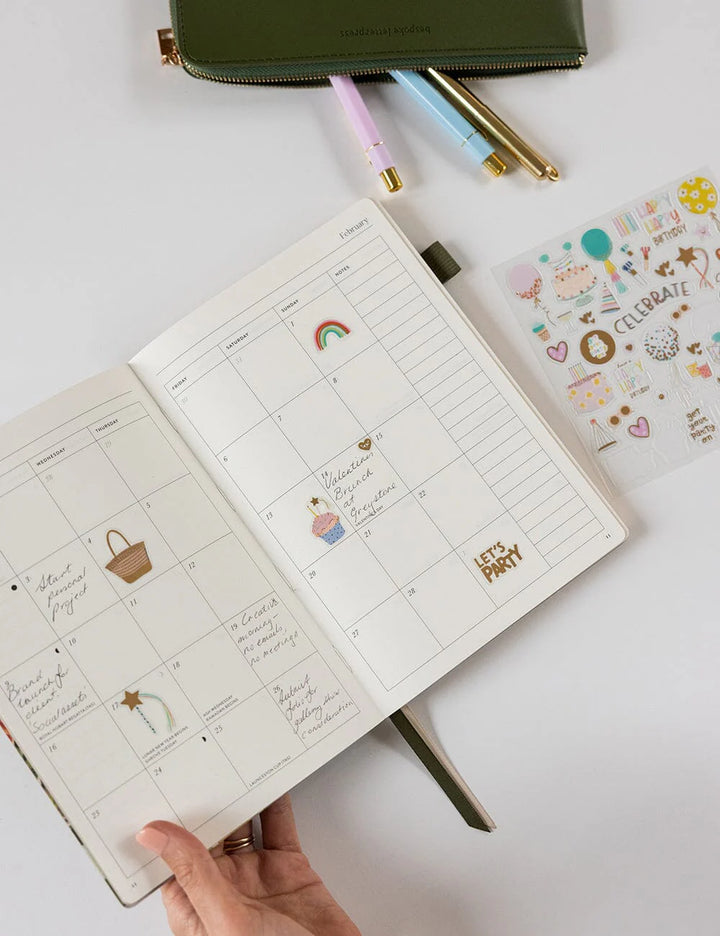 Open planner with stickers and pens on a white surface