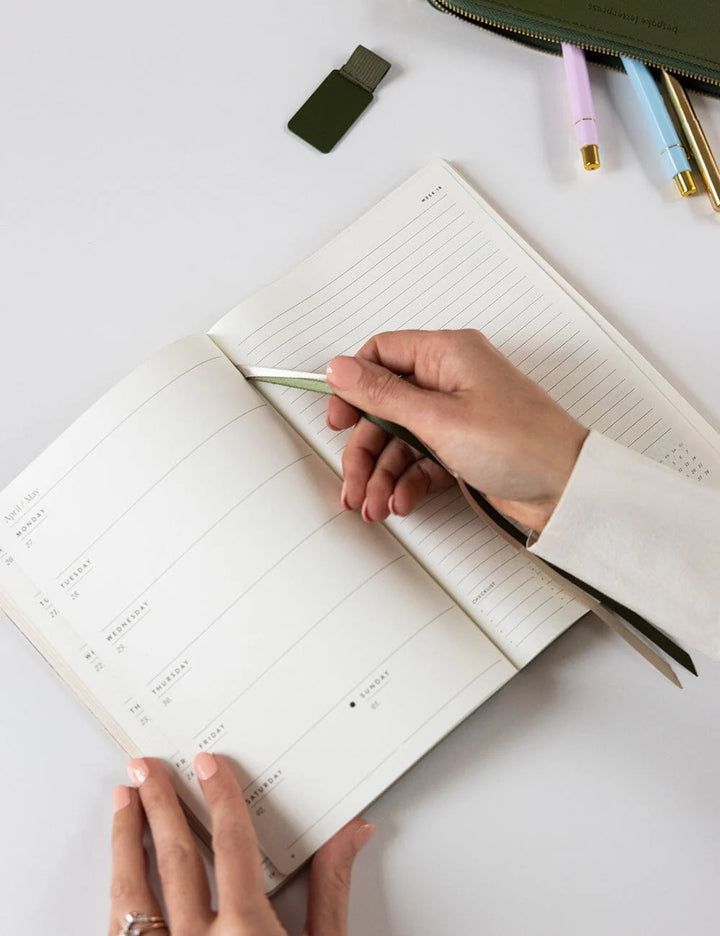 Person writing in a planner with a pen on a white surface