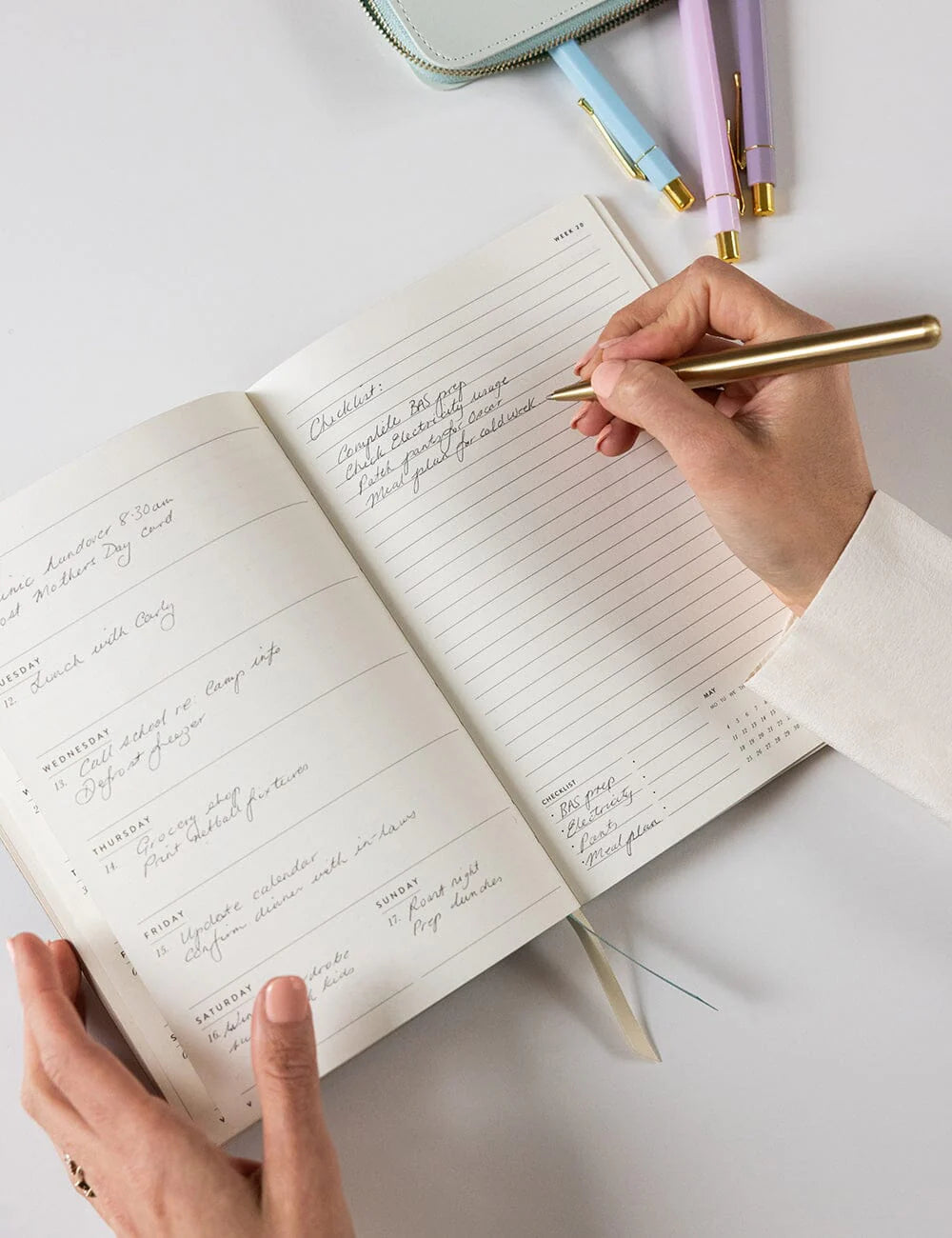 Person writing in a notebook with a gold pen on a light surface.
