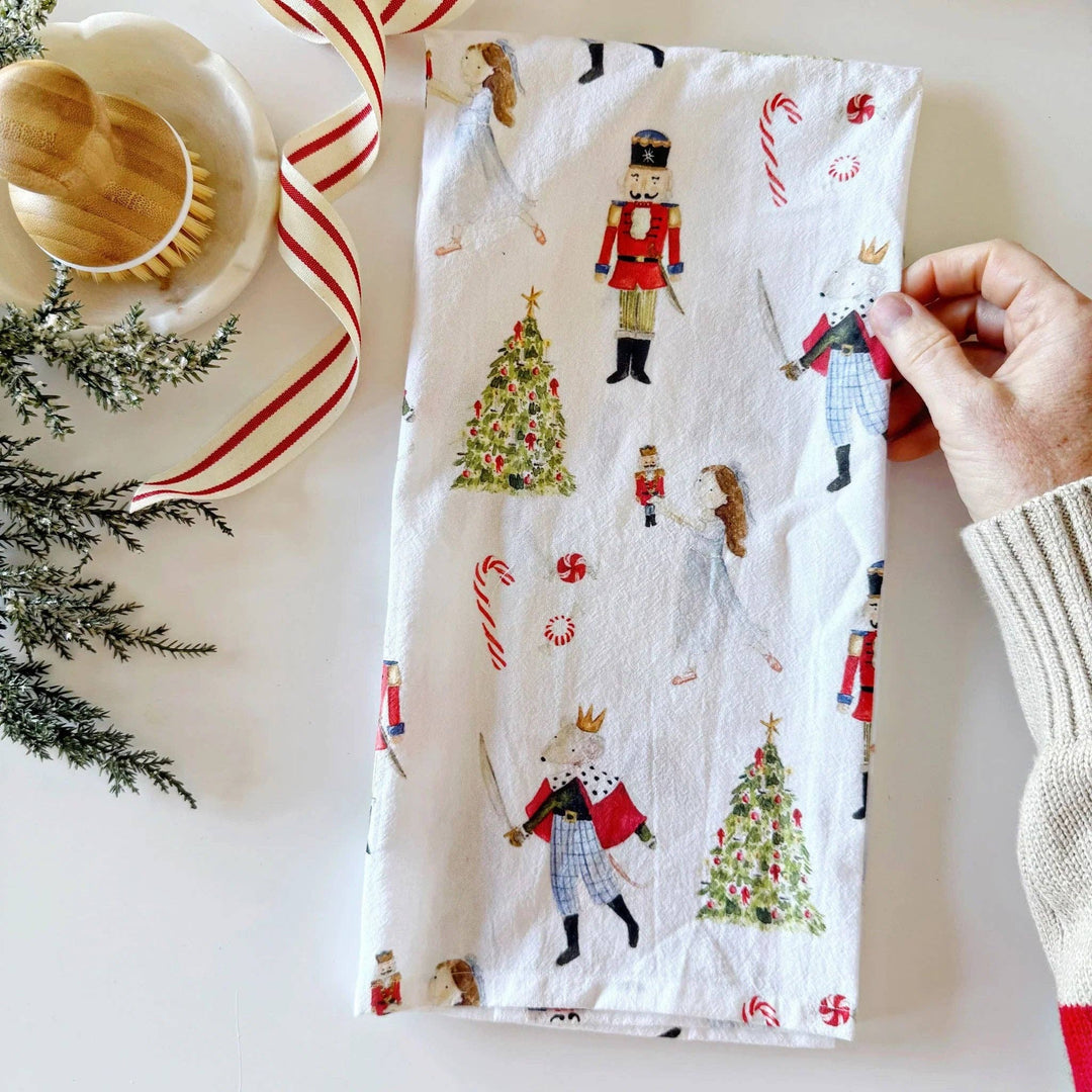 Hand holding a Christmas-themed towel with nutcrackers, trees, and candy canes on a white background.