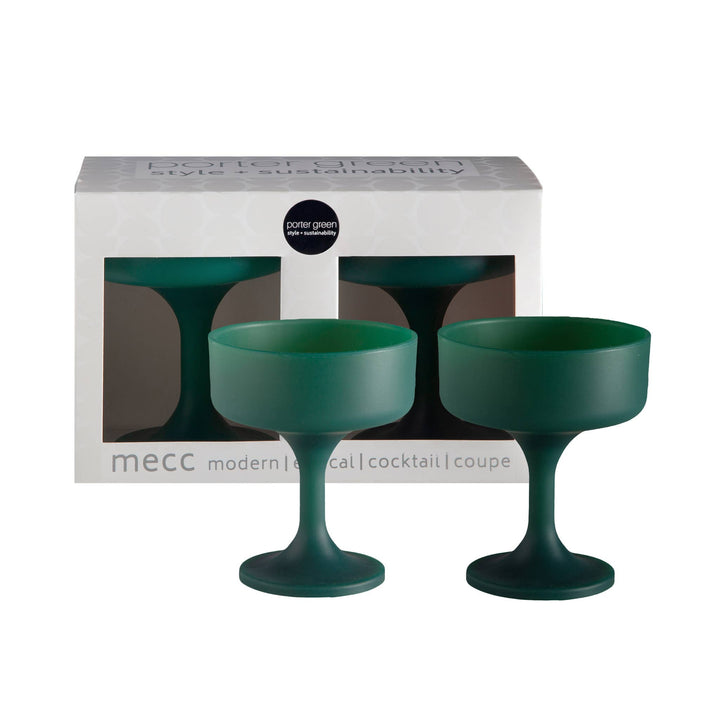 Two dark green silicone coupe glasses displayed in front of their white and gray packaging box, which features the &