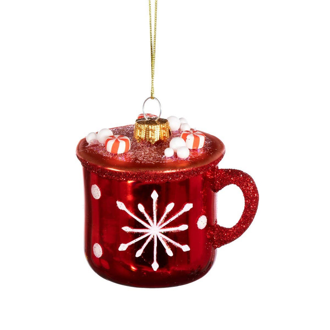 A red glitter Christmas ornament shaped like a mug filled with red-and-white striped candies, and white dots, hanging from a gold string on a white background.