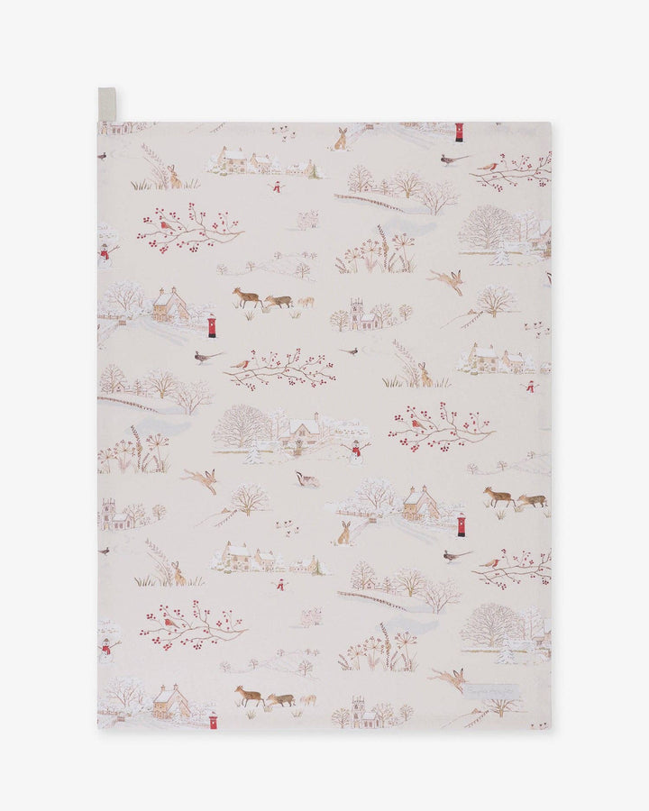A rectangular fabric tea towel, featuring a delicate winter Christmas landscape print on a warm cream background. The pattern includes small houses, trees, birds, and animals in muted brown, red, and blue tones.
