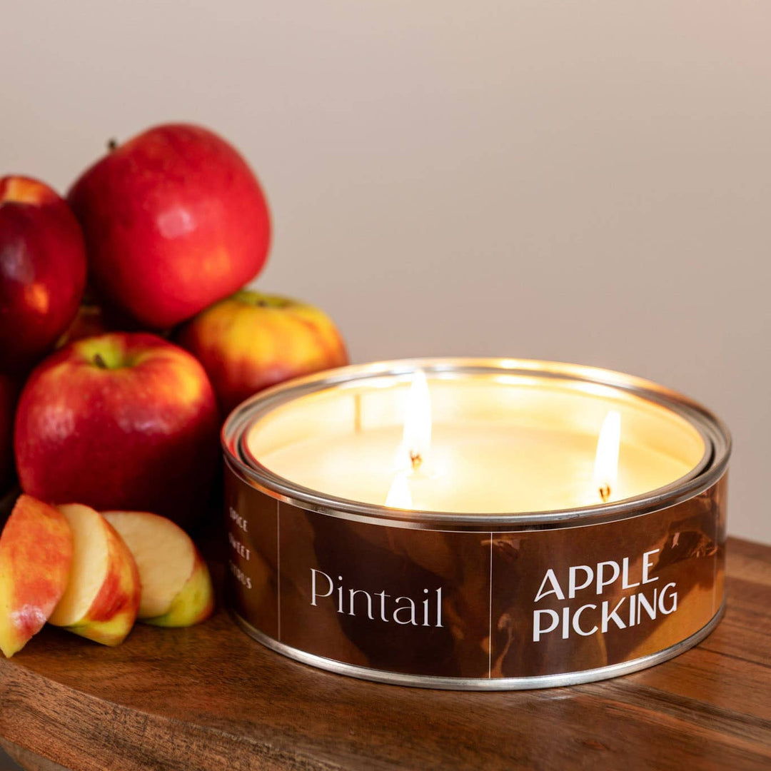 A lit candle in a round metal tin labeled &