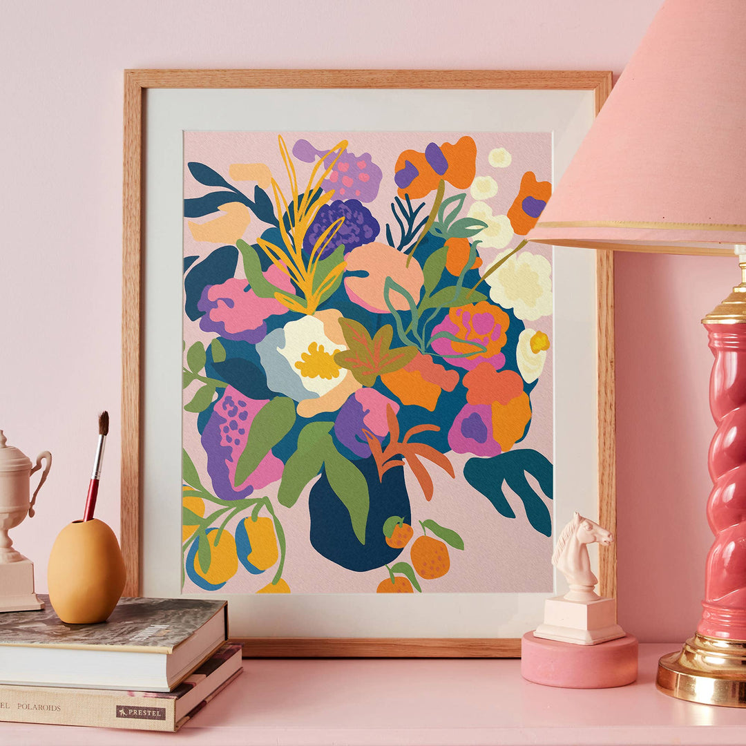 Framed colorful floral artwork on a pink wall with decorative items.