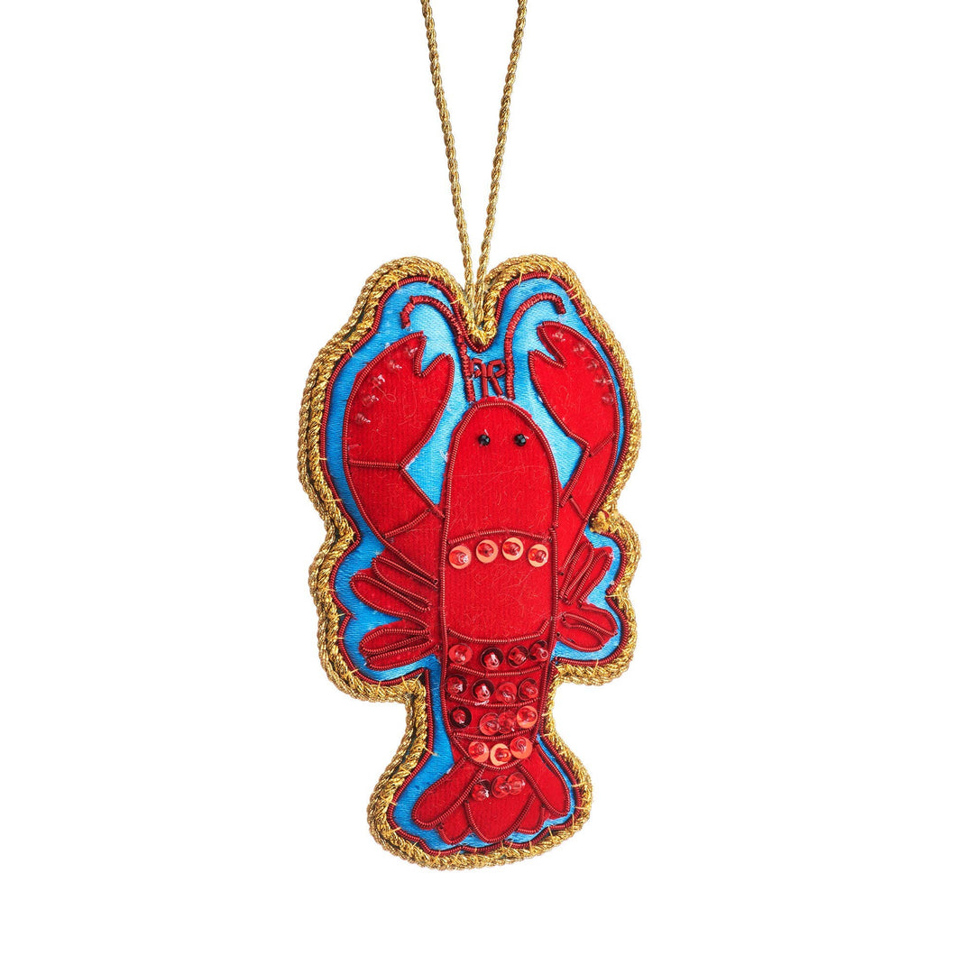 A lobster-shaped fabric ornament or decoration featuring a red lobster body with blue accents, a gold braided border, and a gold hanging string, shown on a plain white background.