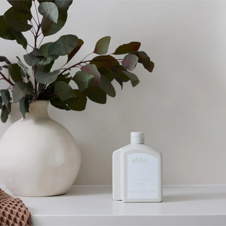 White vase with green leaves and a white bottle on a light surface against a plain background