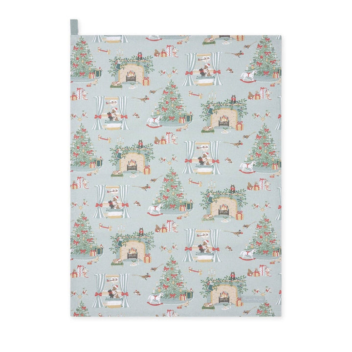 A rectangular fabric tea towel, featuring a festive Christmas pattern on a light blue-gray background. The pattern includes Christmas trees, stockings, fireplaces with Santa Claus, and small birds.