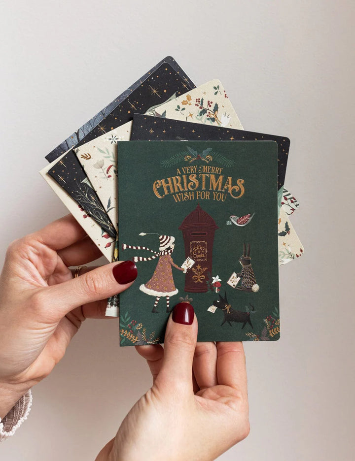 Hand holding a stack of Christmas-themed cards against a neutral background