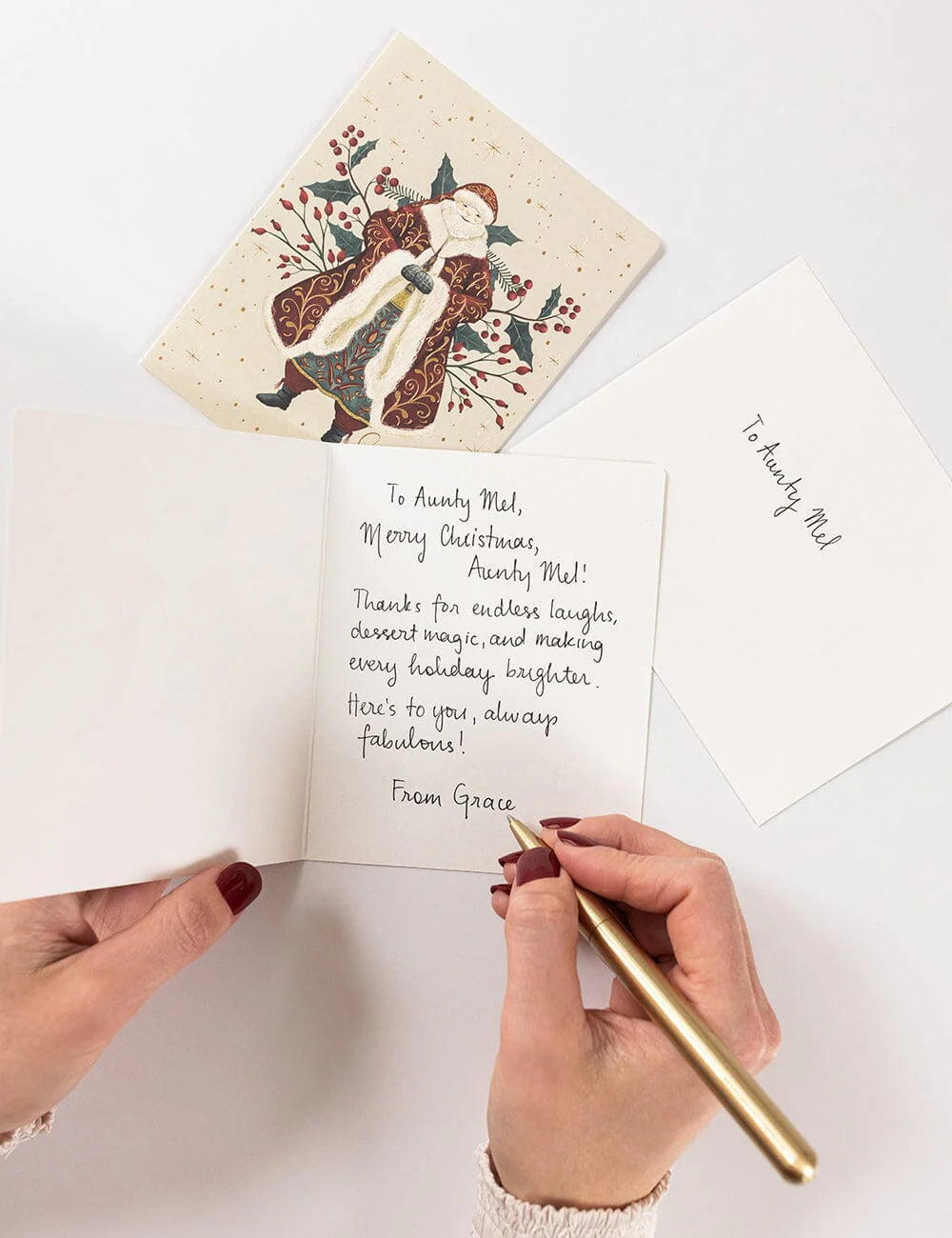 Person writing a personalized message on a Christmas card with a decorative design.