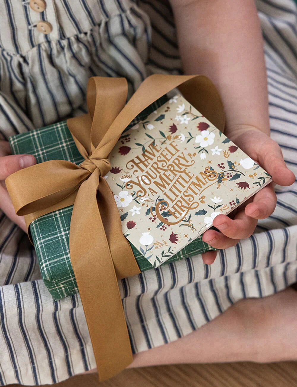 Person holding a small gift box with a decorative ribbon and festive design.