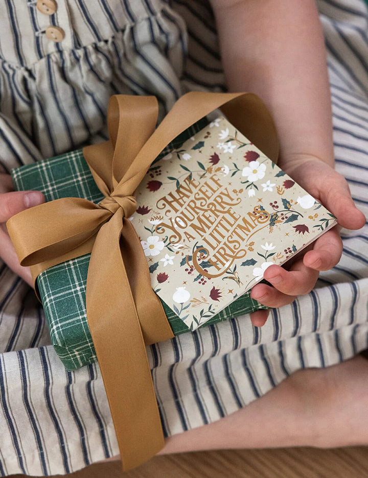 Person holding a small gift box with a decorative ribbon and festive design.
