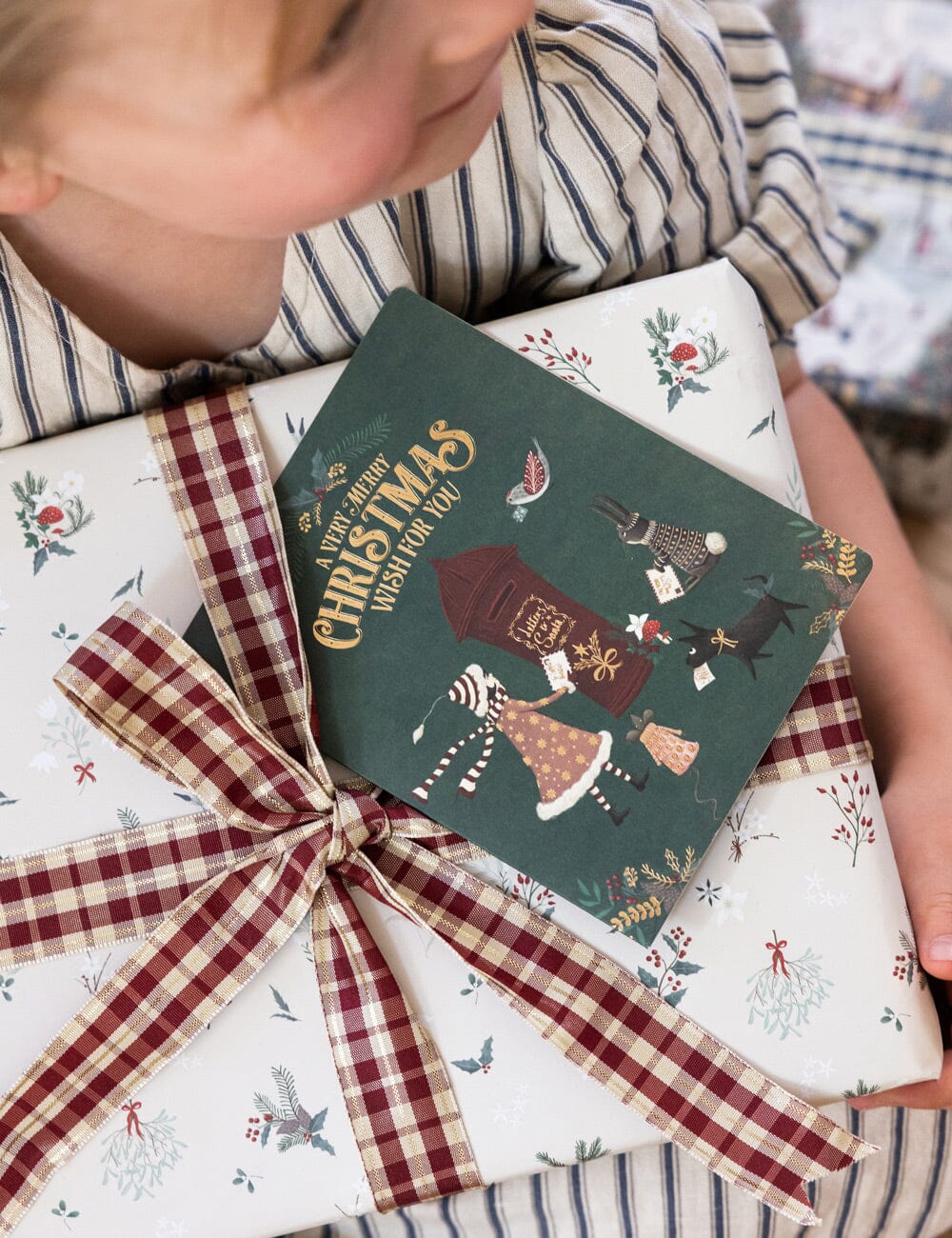 Child opening a Christmas gift wrapped in festive paper with a decorative bow.