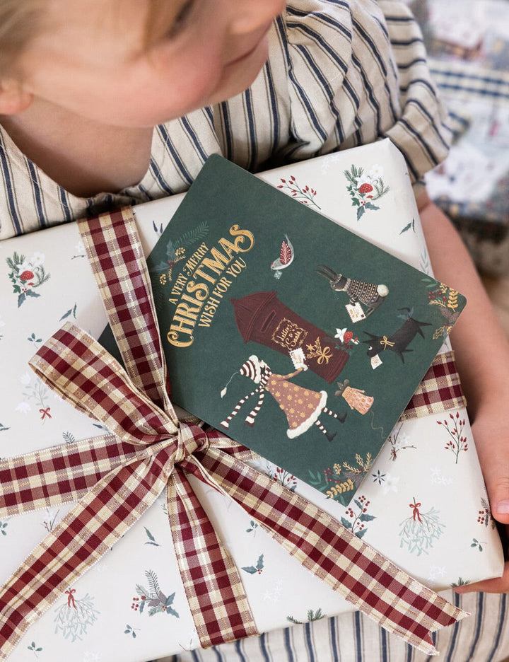 Child opening a Christmas gift wrapped in festive paper with a decorative bow.
