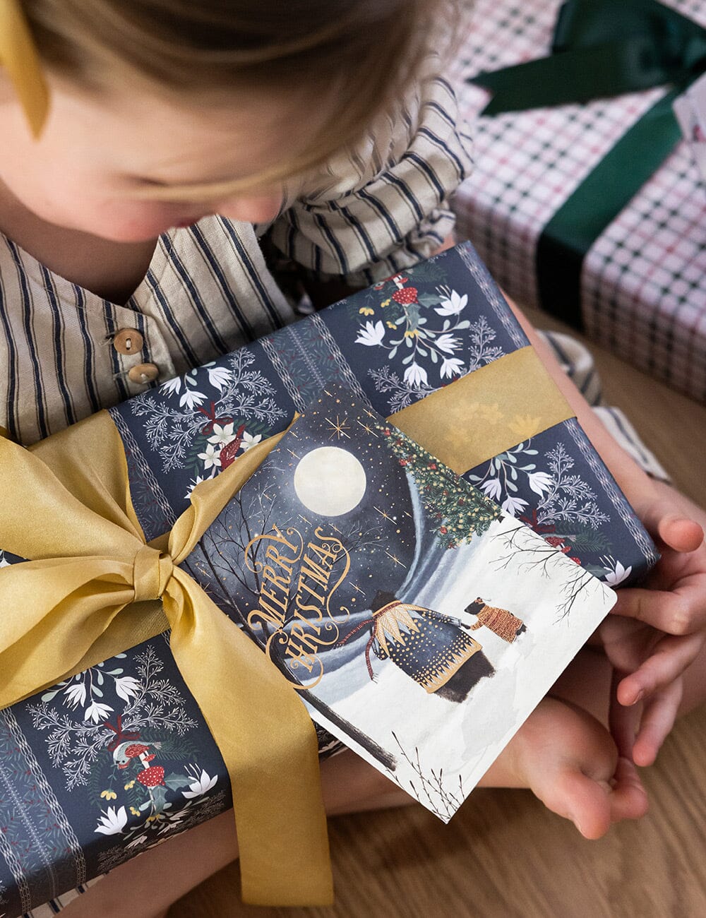 Child holding a beautifully wrapped Christmas gift with decorative paper and ribbon.