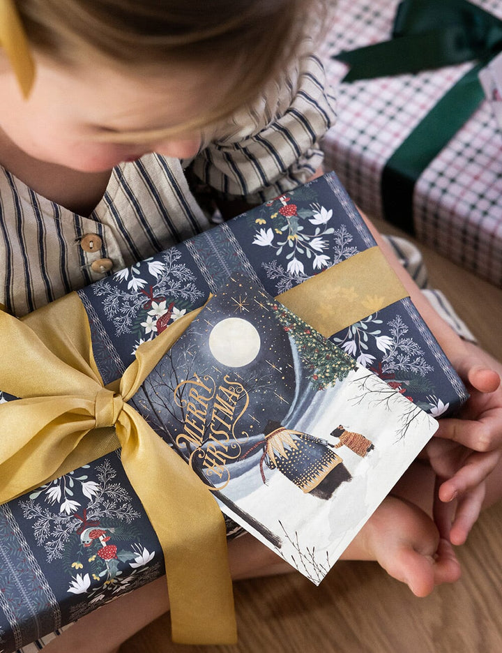 Child holding a beautifully wrapped Christmas gift with decorative paper and ribbon.