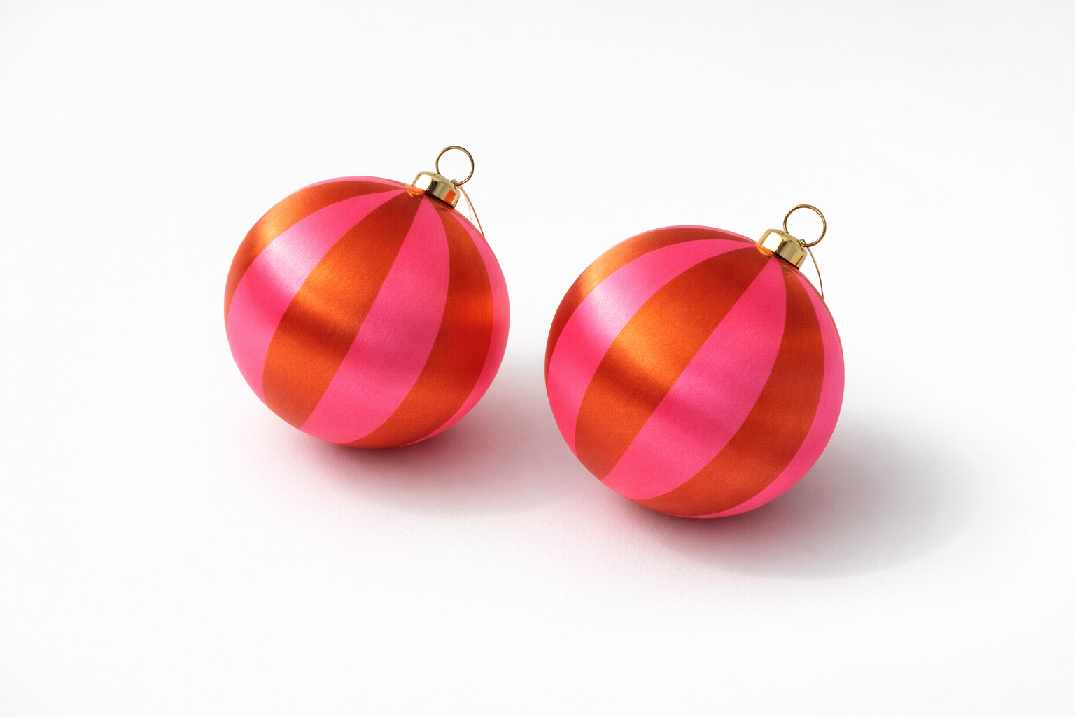 Two round Christmas ornaments with metallic pink and orange-red vertical stripes, each with a small gold hanging loop at the top, shown on a clean white background.