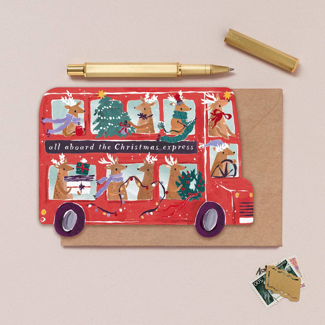Christmas-themed card with a red bus and reindeer design on a beige background.