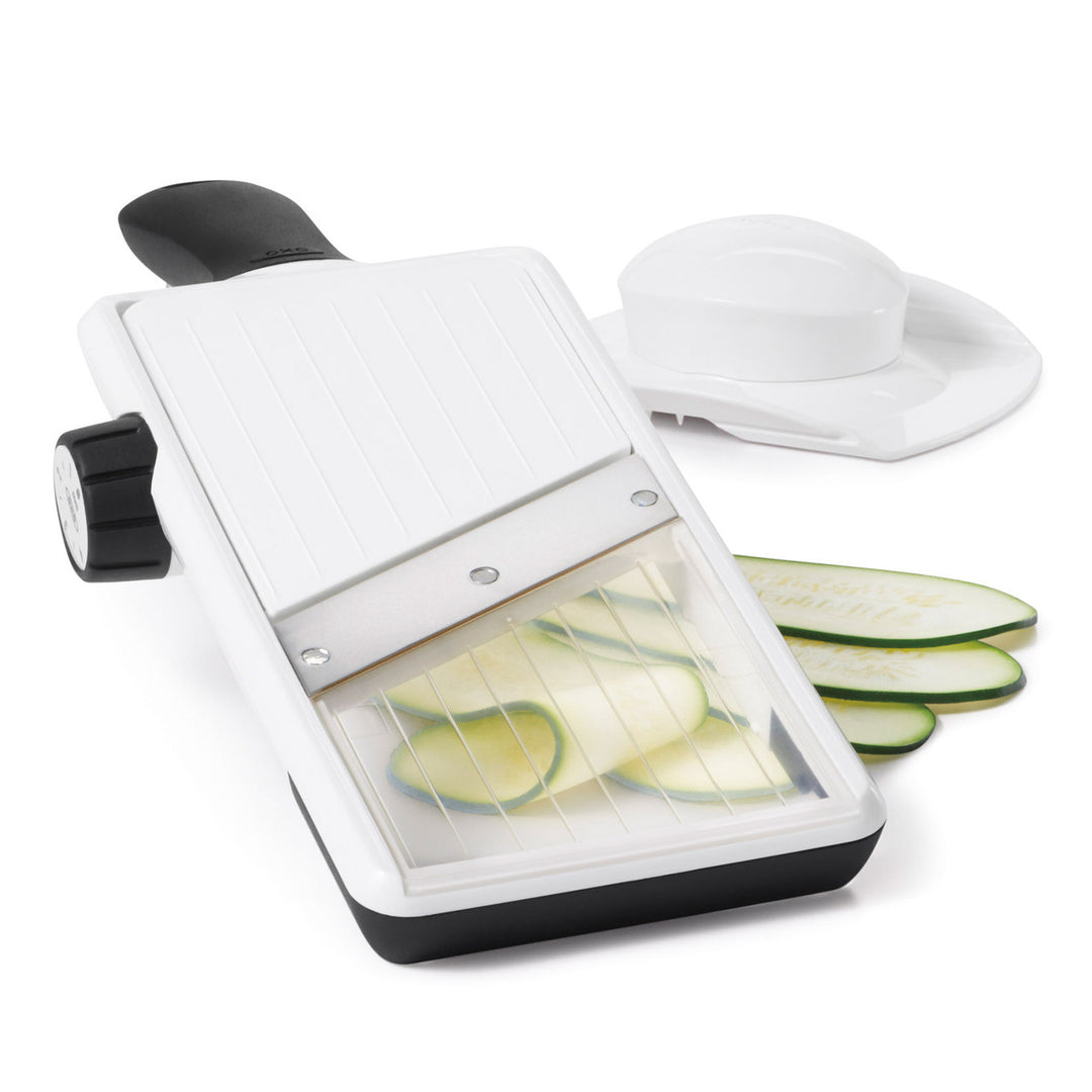 White mandoline slicer with sliced zucchinis on a white background