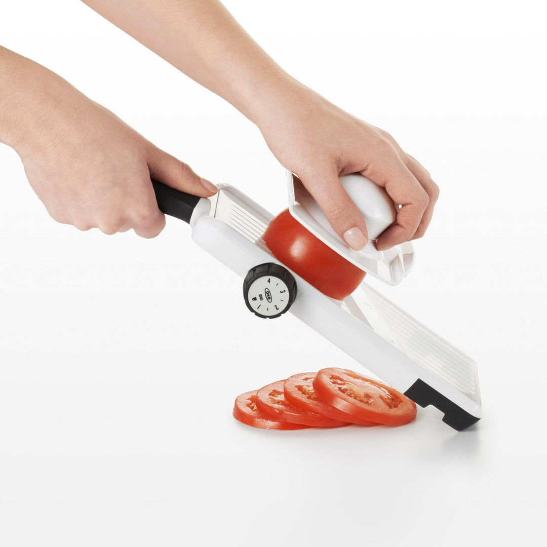 Handheld mandoline slicer with sliced tomatoes on a white background