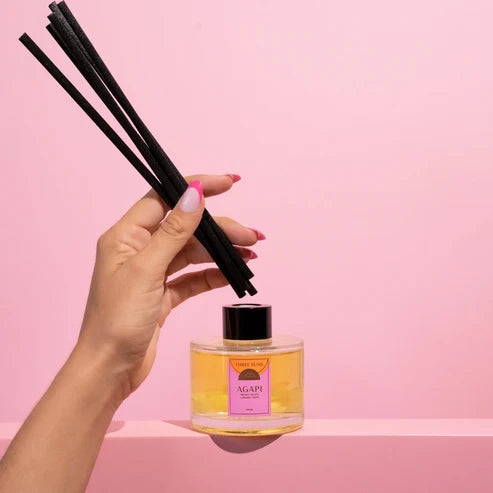Hand holding a diffuser bottle with black sticks against a pink background