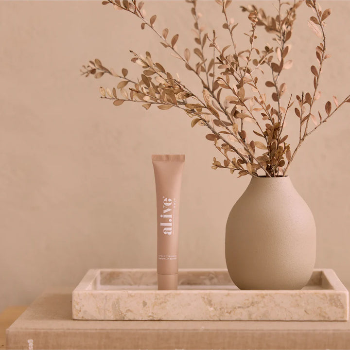 Tube of 'alive' cream on a marble tray with a vase of branches against a beige wall.