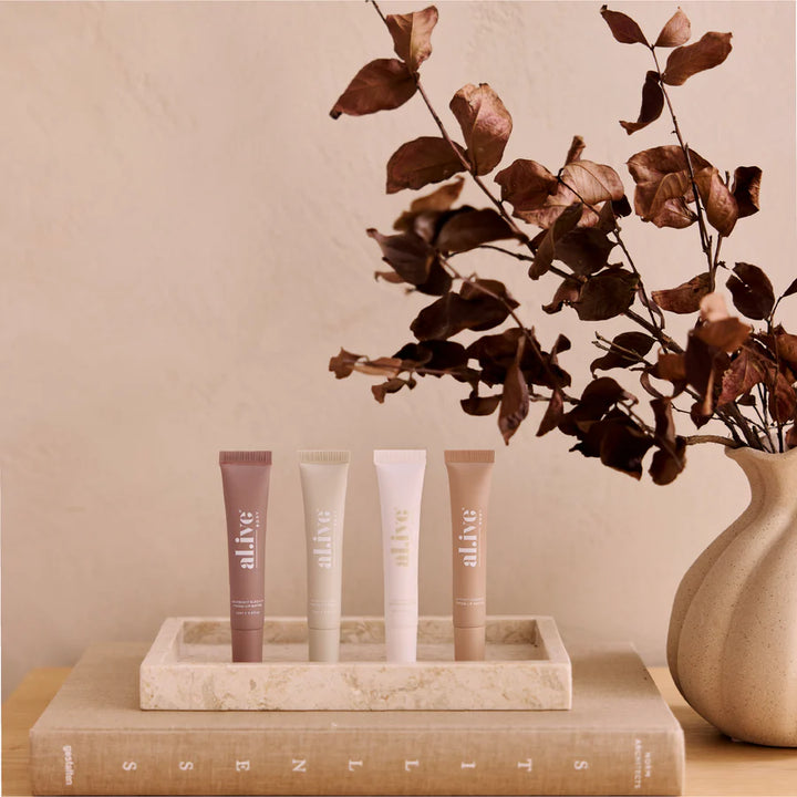 Lip products on a tray with a vase of dried leaves on a beige surface
