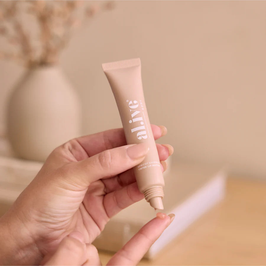 Hand holding a beige cosmetic tube with 'Elle' branding against a neutral background