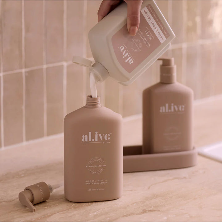 Person pouring a liquid from a white bottle into a beige 'al.ive' bottle on a bathroom counter.