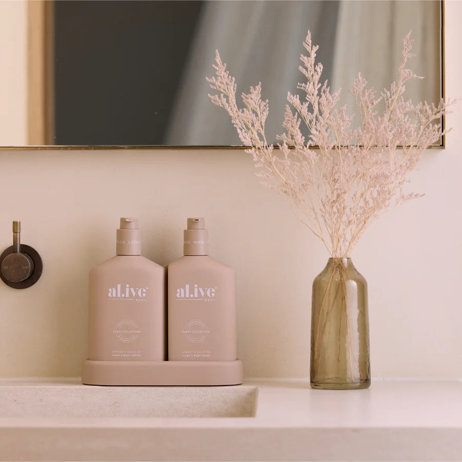 Two beige bottles labeled 'alive' on a shelf with a vase of dried flowers.