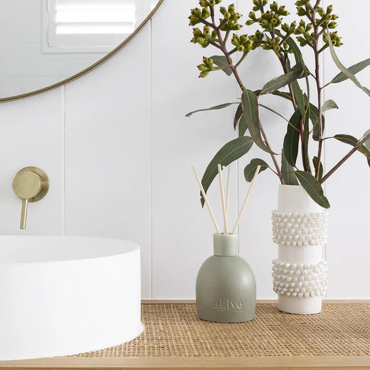Two vases with greenery on a wooden surface in a minimalistic room.