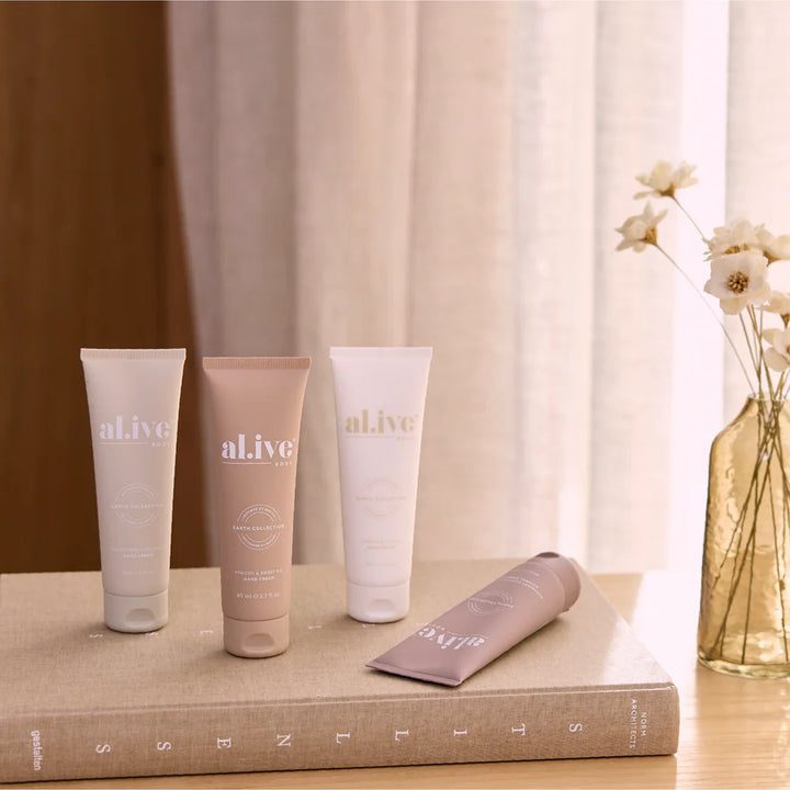 Four 'alive' skincare products on a textured surface with a vase of flowers in the background.