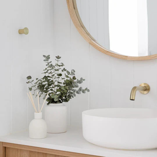 Bathroom vanity with a round mirror, white sink, and decorative plants.