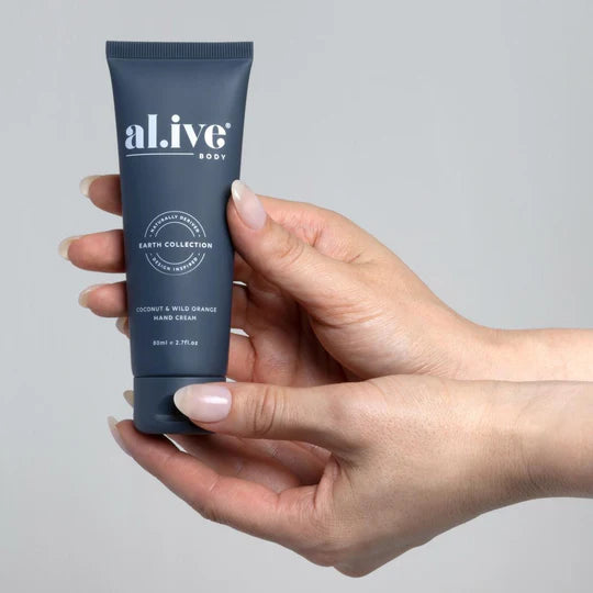 Hand holding a tube of al.ive body hand cream against a gray background