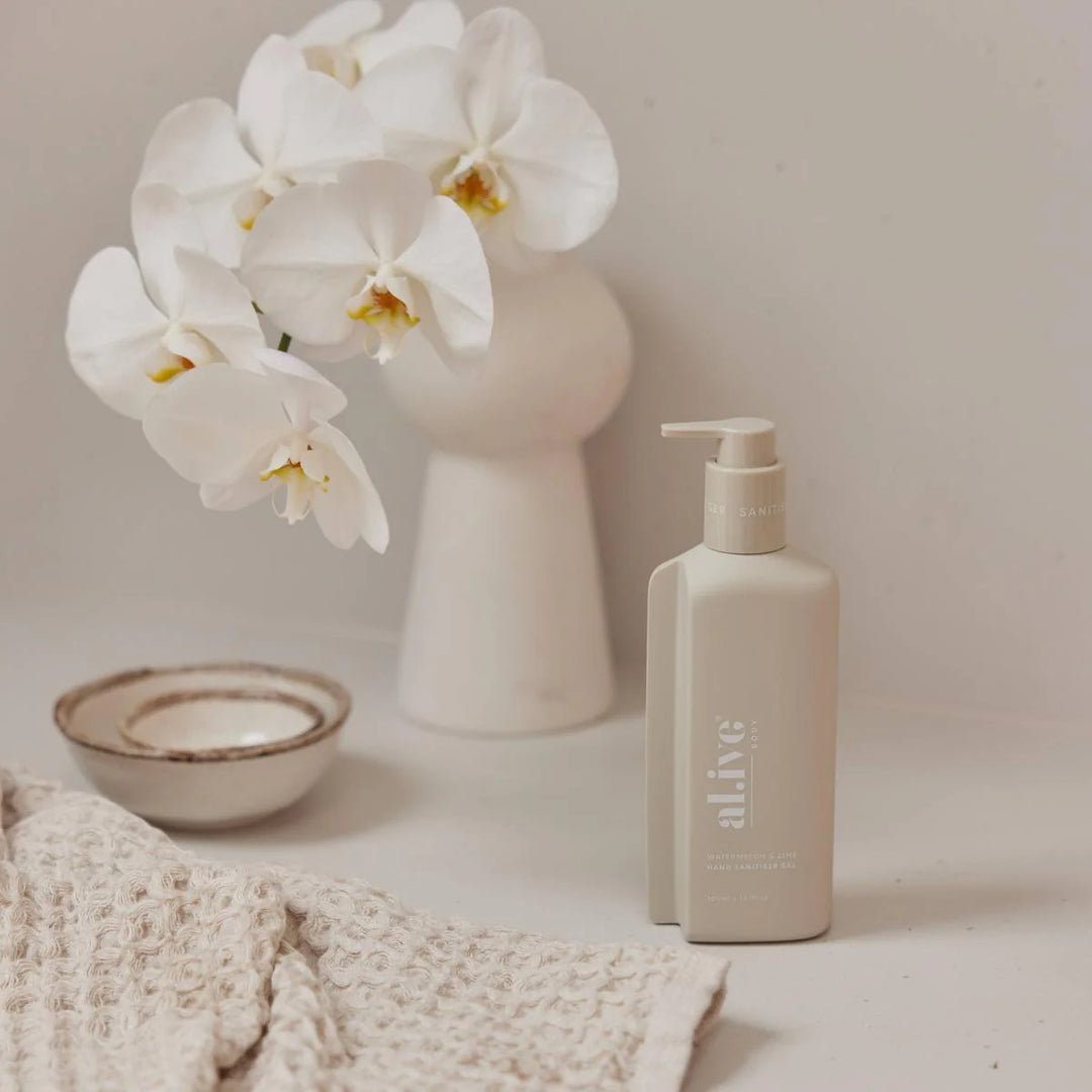Skincare bottle labeled 'alive' next to a vase with white flowers on a neutral background